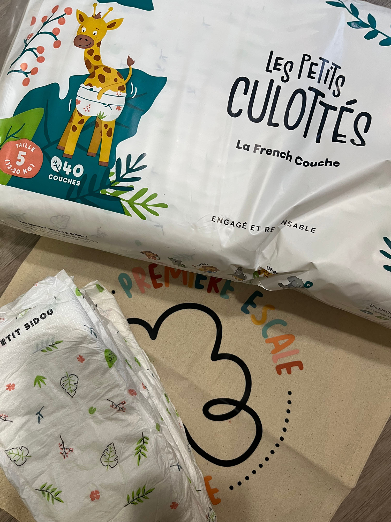 Nouvelles couches écologiques Les Petits Culottés adoptées par la micro-crèche : paquet illustré avec une girafe et couches posées sur un sac Première Escale.