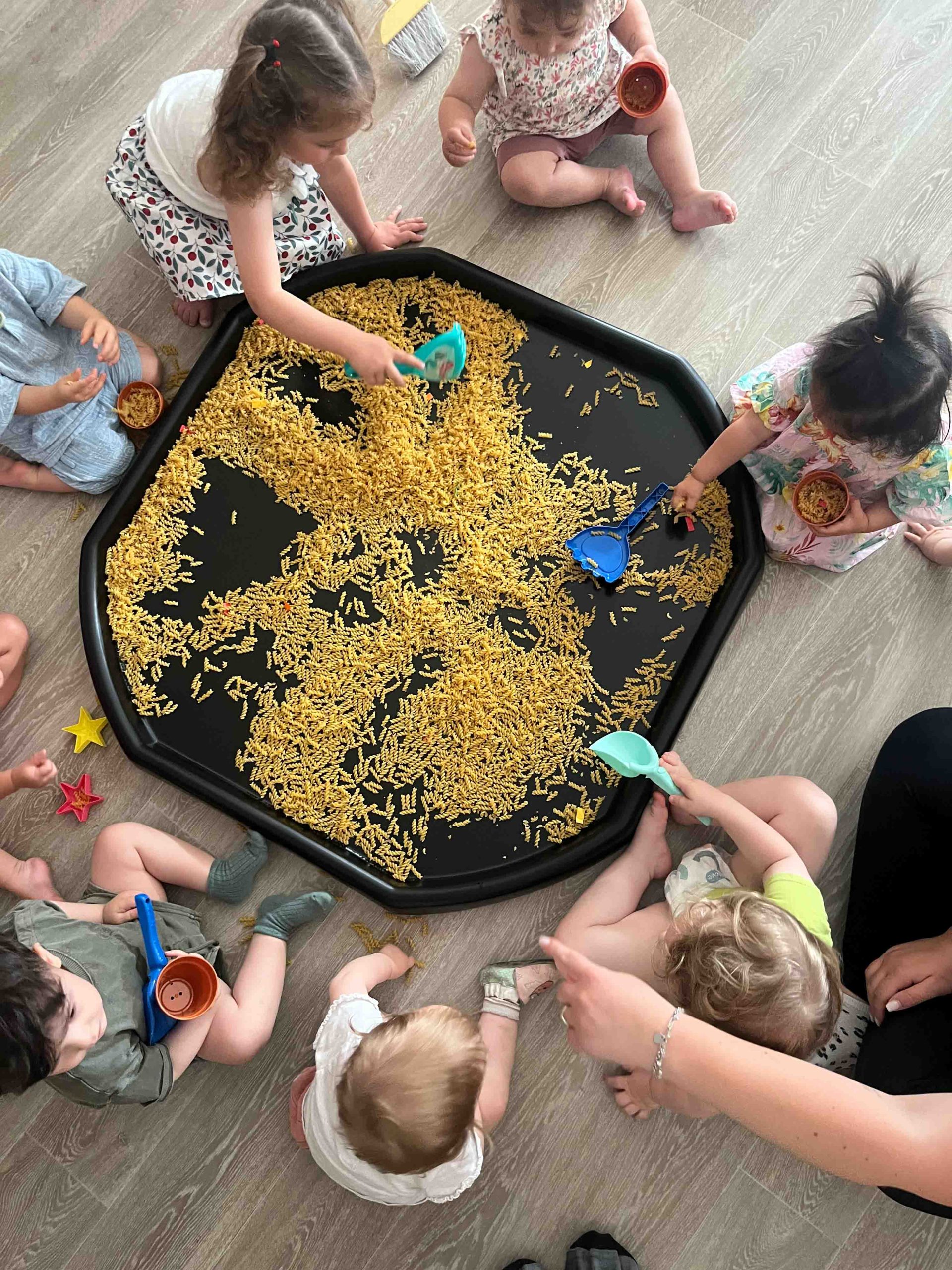 Atelier sensoriel à la micro-crèche première escale de Colmar : des enfants jouent ensemble autour d’un bac rempli de pâtes sèches, favorisant la motricité fine et la découverte tactile.
