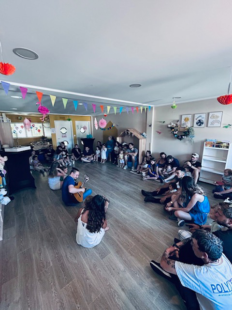 photo de groupe, atelier guitare avec les parents et leurs enfant assis en tailleur autour du guitariste, dans la micro crèche première escale de Colmar